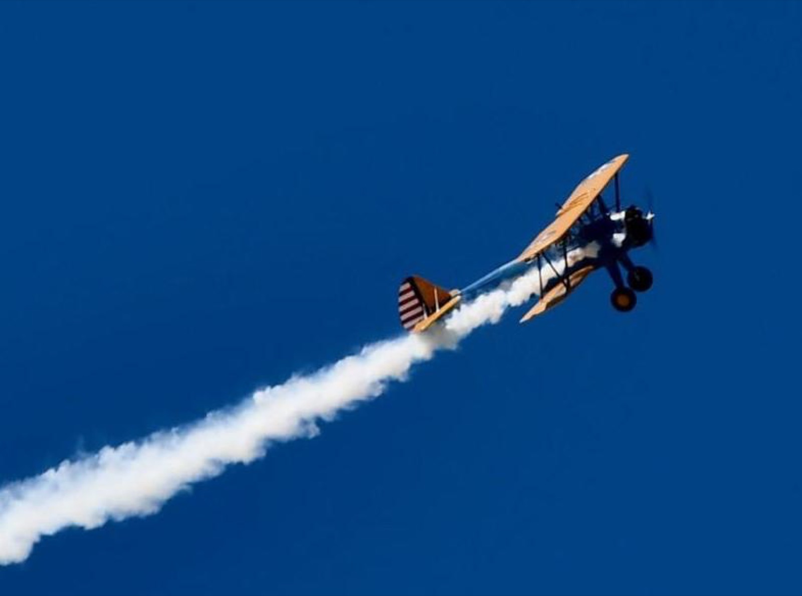 Stearman climbing with a smoke trail against a deep blue sky